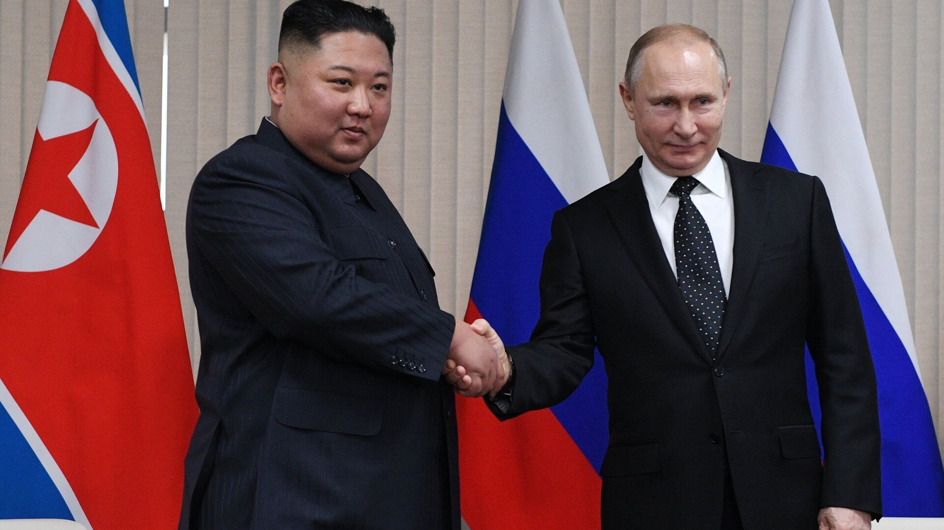 Poignée de main entre Kim Jong-un et Vladimir Poutine devant les drapeaux nord-coréen et russe.