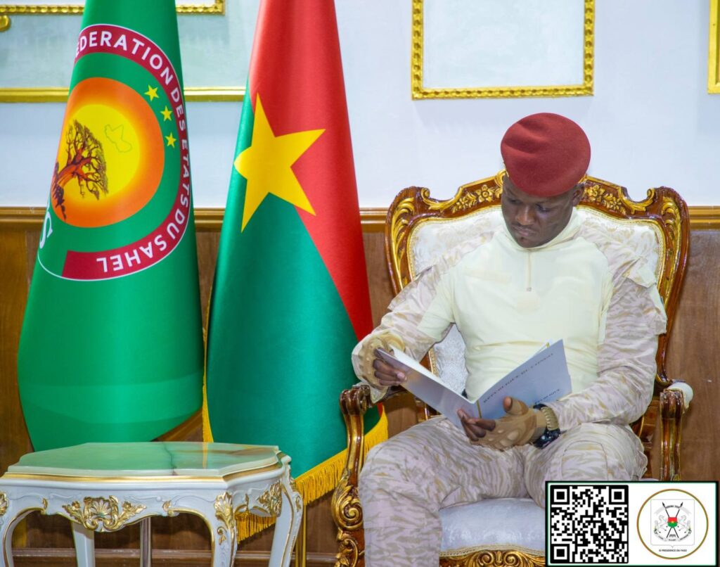 Le Président du Faso, Ibrahim Traoré, lisant un document officiel, assis entre les drapeaux du Burkina Faso et de la Fédération des États du Sahel.