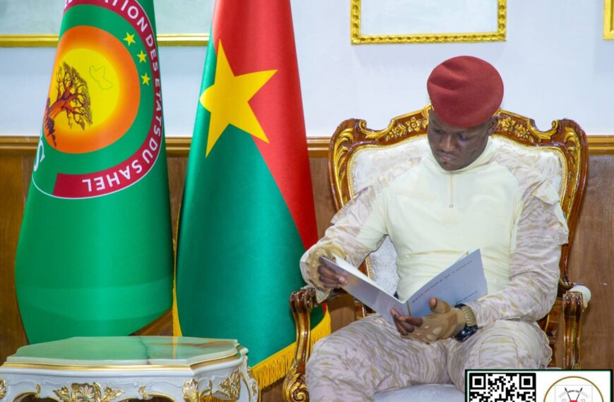 Le Président du Faso, Ibrahim Traoré, lisant un document officiel, assis entre les drapeaux du Burkina Faso et de la Fédération des États du Sahel.