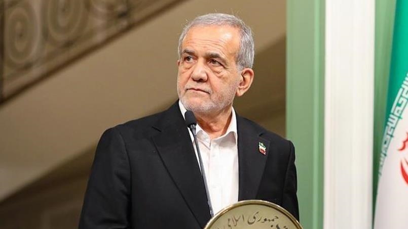 Le président iranien s’exprime devant un micro, debout près du drapeau national.