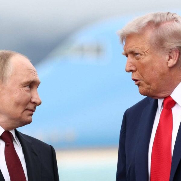 Vladimir Poutine et Donald Trump discutant face à face sur un tarmac, avec un avion flou en arrière-plan.