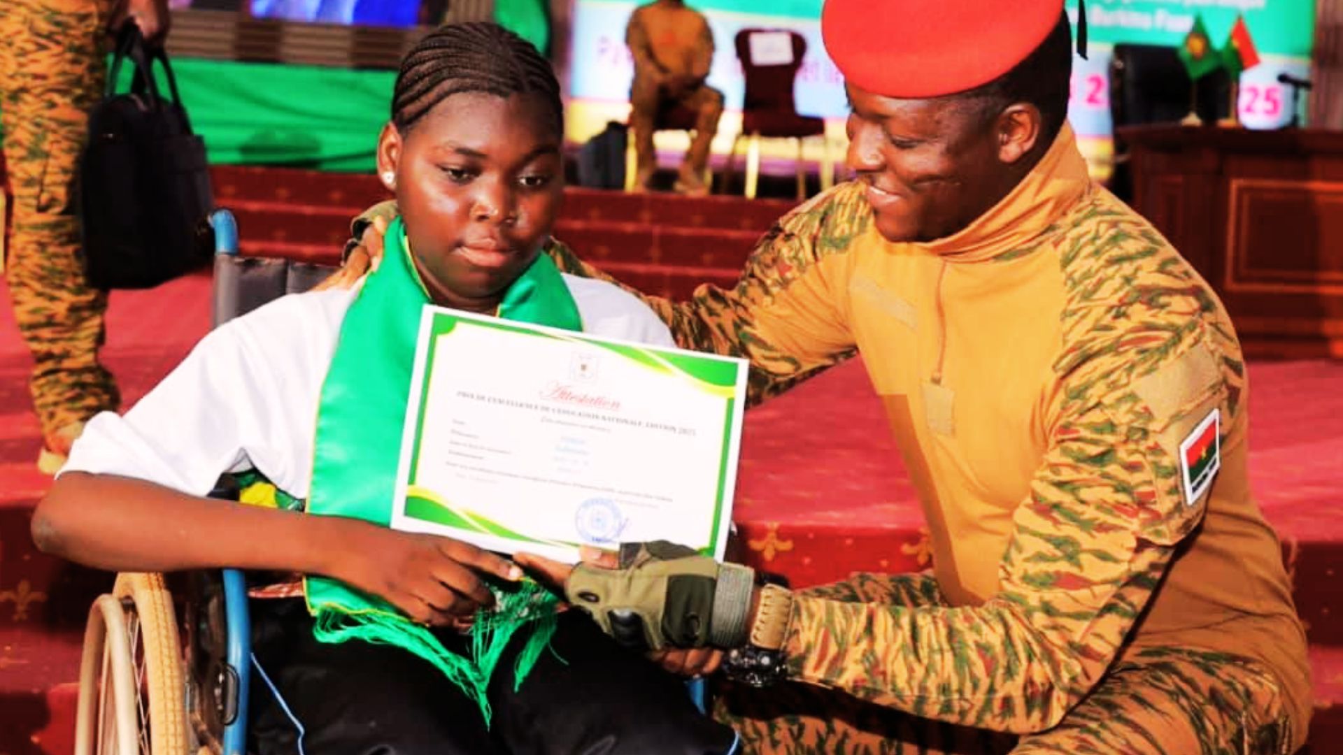 Une élève en fauteuil roulant reçoit un certificat d’excellence des mains d’un militaire burkinabè en uniforme.