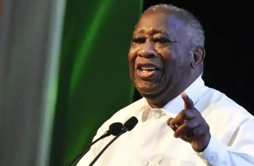Laurent Gbagbo prononçant un discours, vêtu d’une chemise blanche, souriant et pointant du doigt.