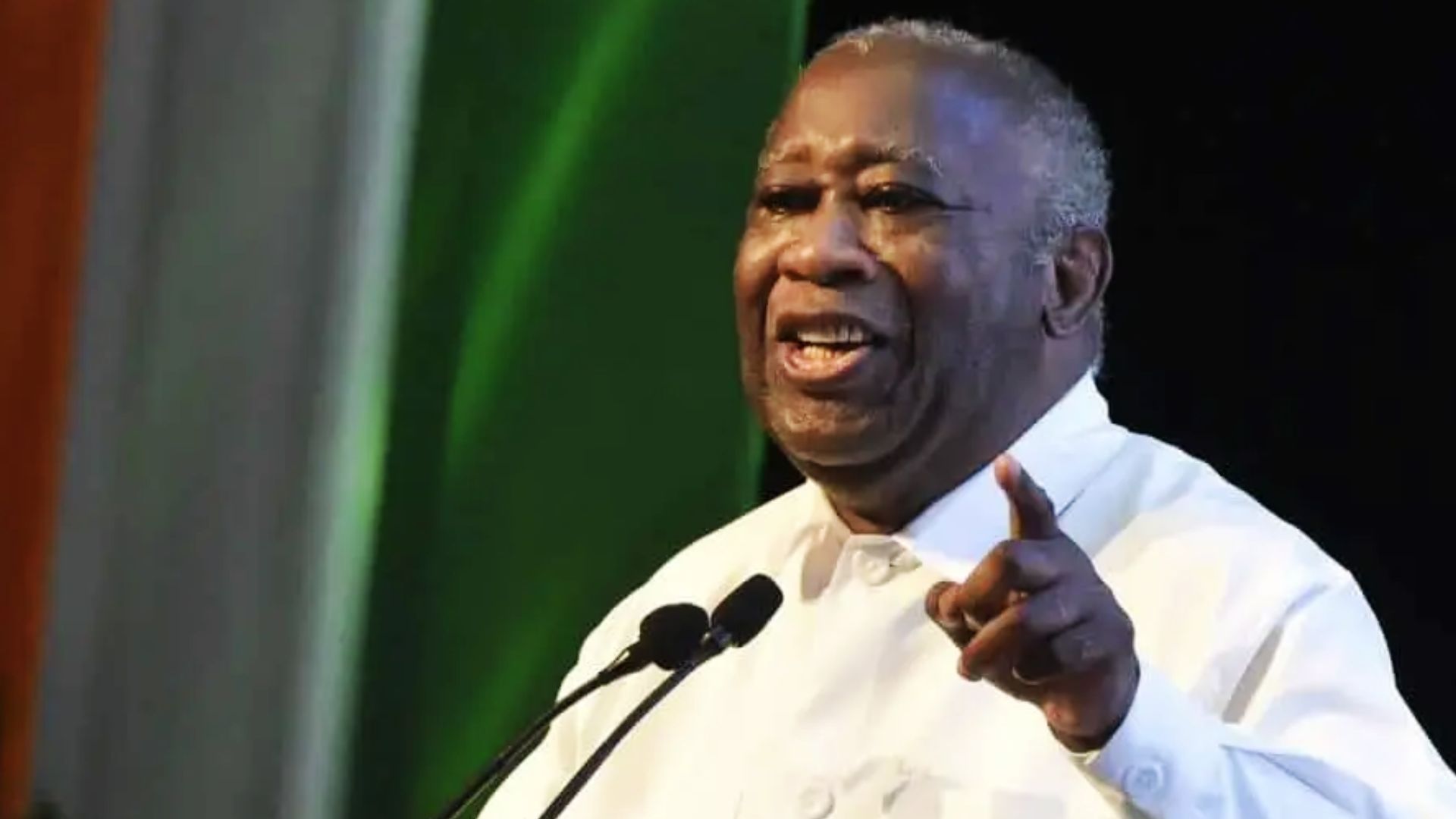 Laurent Gbagbo prononçant un discours, vêtu d’une chemise blanche, souriant et pointant du doigt.