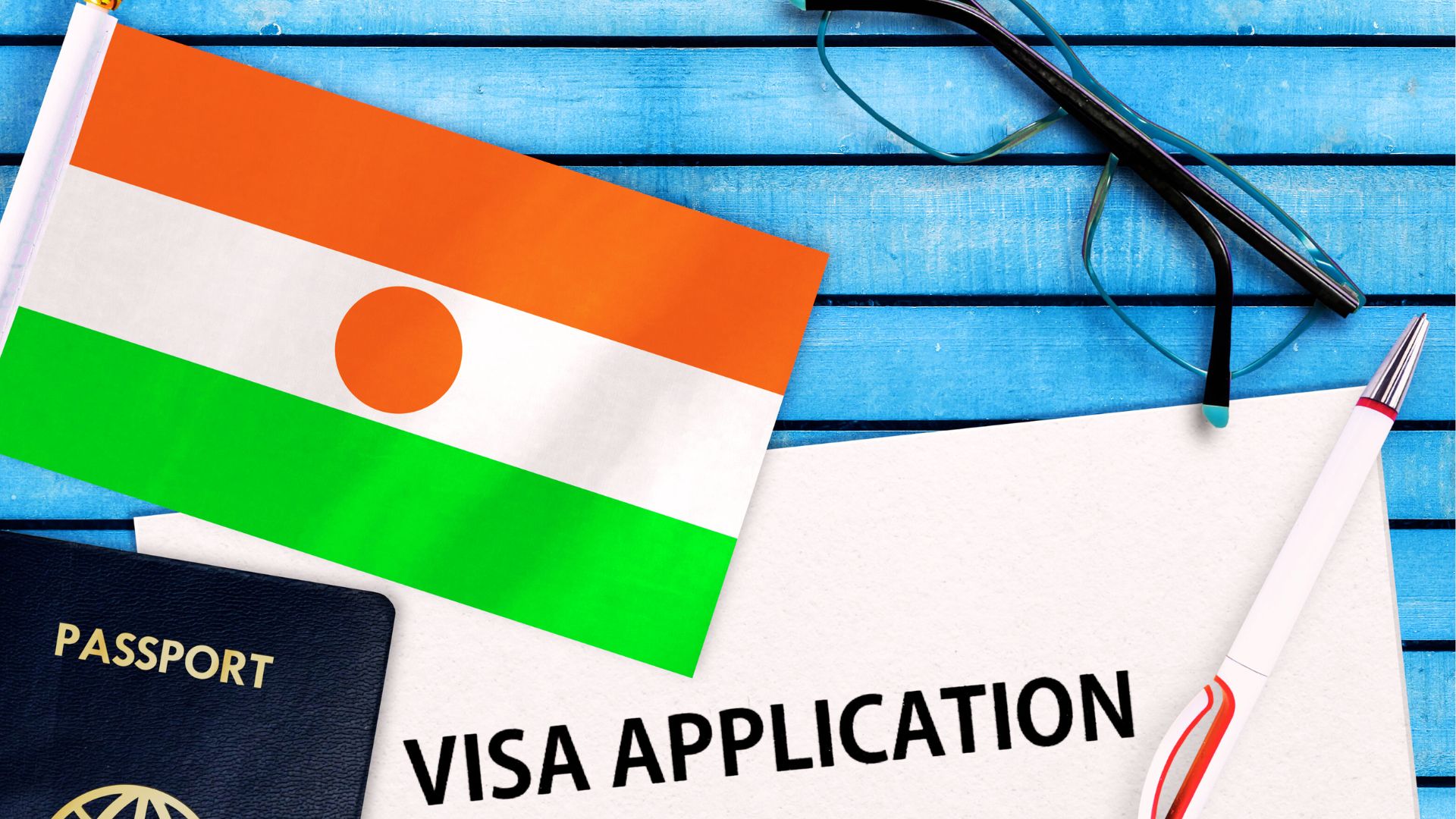 Drapeau du Niger posé sur une table en bois bleu, à côté d’un passeport, d’un formulaire de demande de visa et d’un stylo.