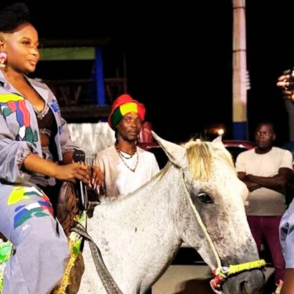 Une artiste haïtienne défile à cheval lors d’un événement nocturne, vêtue d’une tenue colorée et entourée de spectateurs
