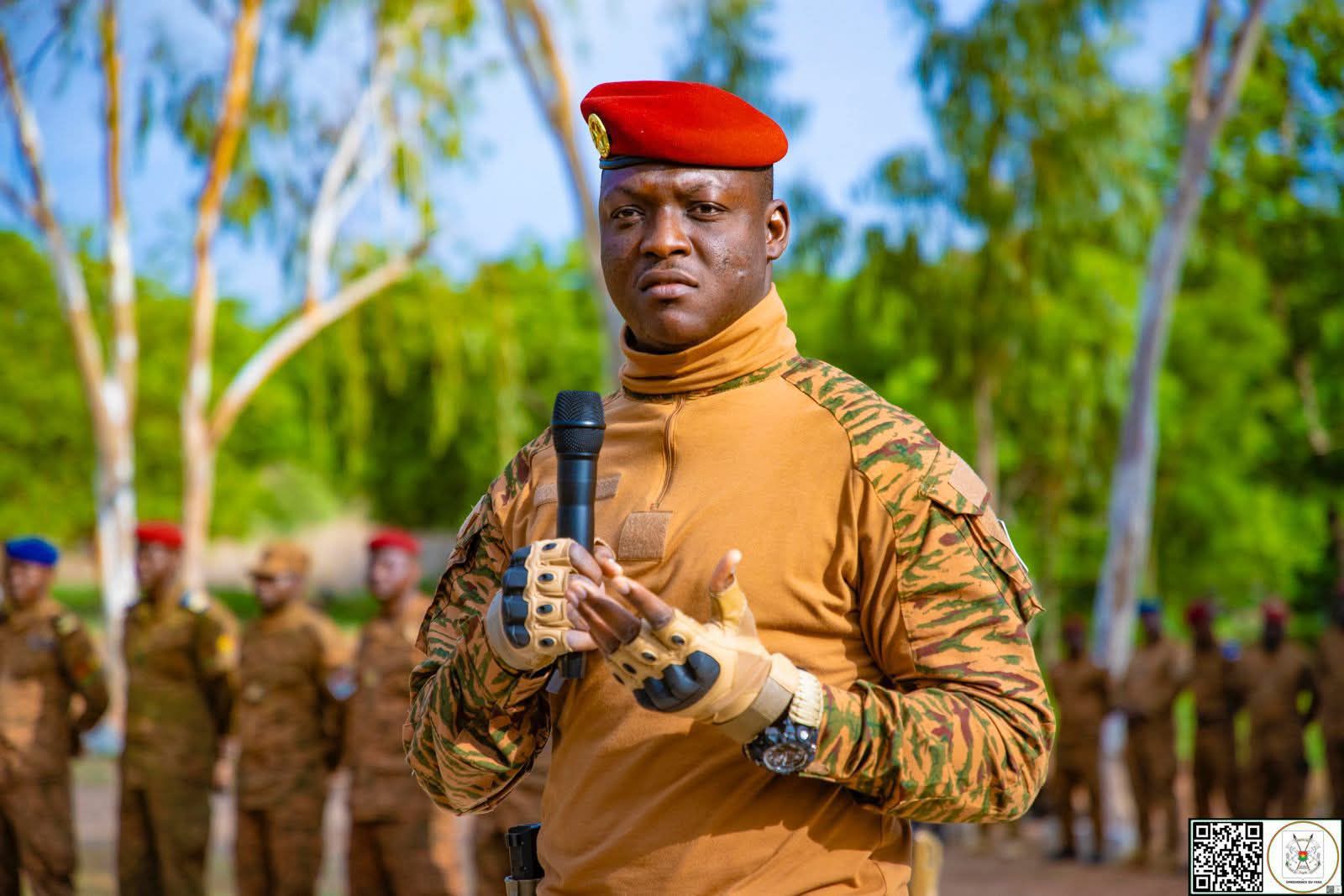 Le capitaine Ibrahim Traoré en tenue militaire, tenant un micro, s'adressant à des soldats alignés en arrière-plan.