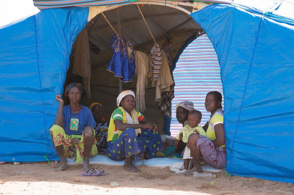 Femmes déplacées et enfants assis à l’entrée d’un abri en toile bleue au Burkina Faso.