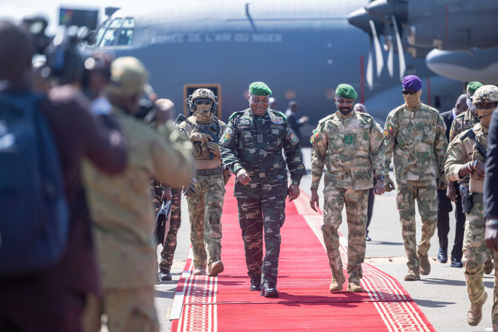 Assimi Goïta et Abdourahamane Tiani marchent sur un tapis rouge à l’aéroport, entourés de militaires.