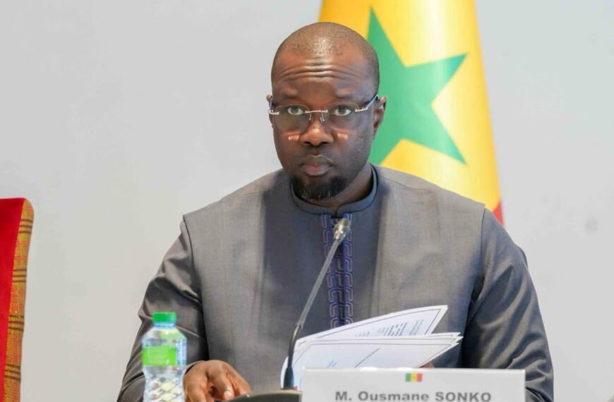 Ousmane Sonko, Premier ministre du Sénégal, lors d’une conférence à Dakar, avec le drapeau sénégalais en arrière-plan.