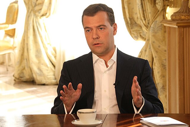 Dmitri Medvedev lors d’une interview à Sotchi en 2008, assis à une table, mains levées dans un geste explicatif.