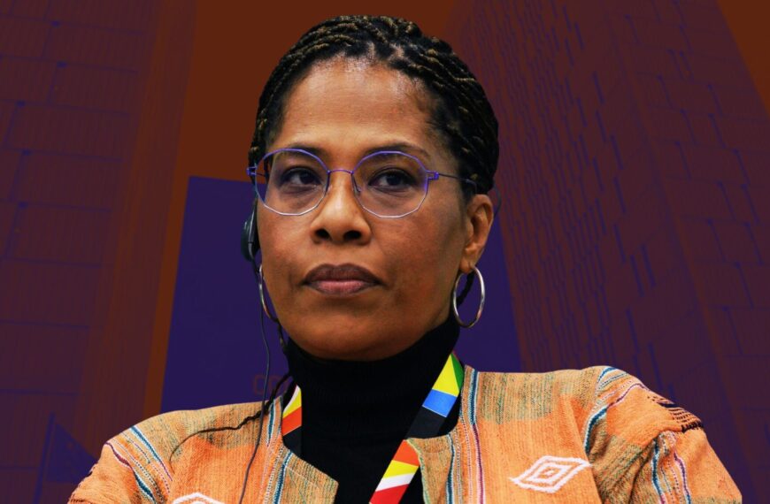 Portrait de Nathalie Yamb, militante panafricaine, portant des lunettes et une tenue traditionnelle, sur un fond aux tons rouges et violets.
