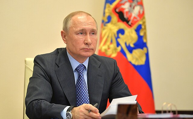 Le président russe assis à son bureau, tenant des documents officiels, devant le drapeau national.