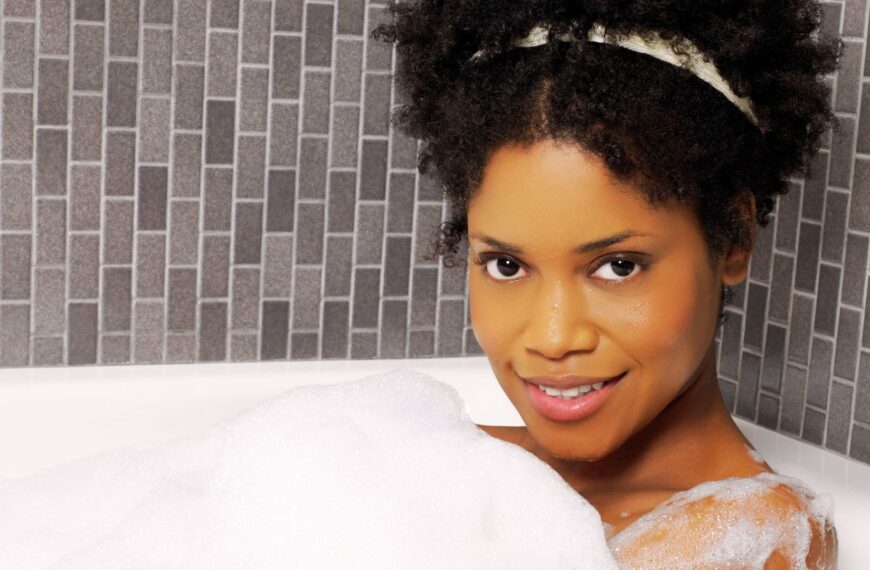 Une jeune femme sort d’une douche froide, ruisselante d’eau, respirant profondément pour se réchauffer, symbole de vitalité et de bien-être naturel.