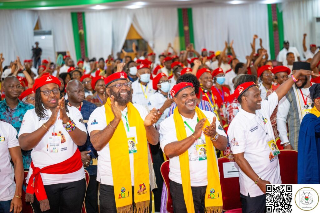 Groupe de participants applaudissant dans une salle de conférence décorée en rouge, vert et blanc.