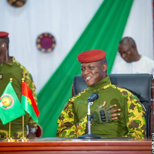 Le capitaine Ibrahim Traoré assis derrière un bureau, en tenue militaire, devant des drapeaux posés sur la table lors d’une rencontre officielle.