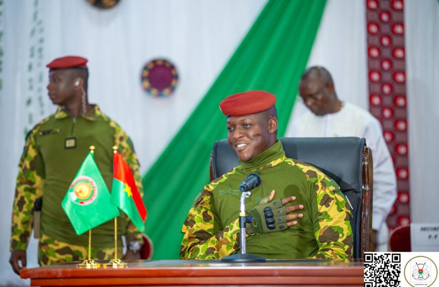 Le capitaine Ibrahim Traoré assis derrière un bureau, en tenue militaire, devant des drapeaux posés sur la table lors d’une rencontre officielle.