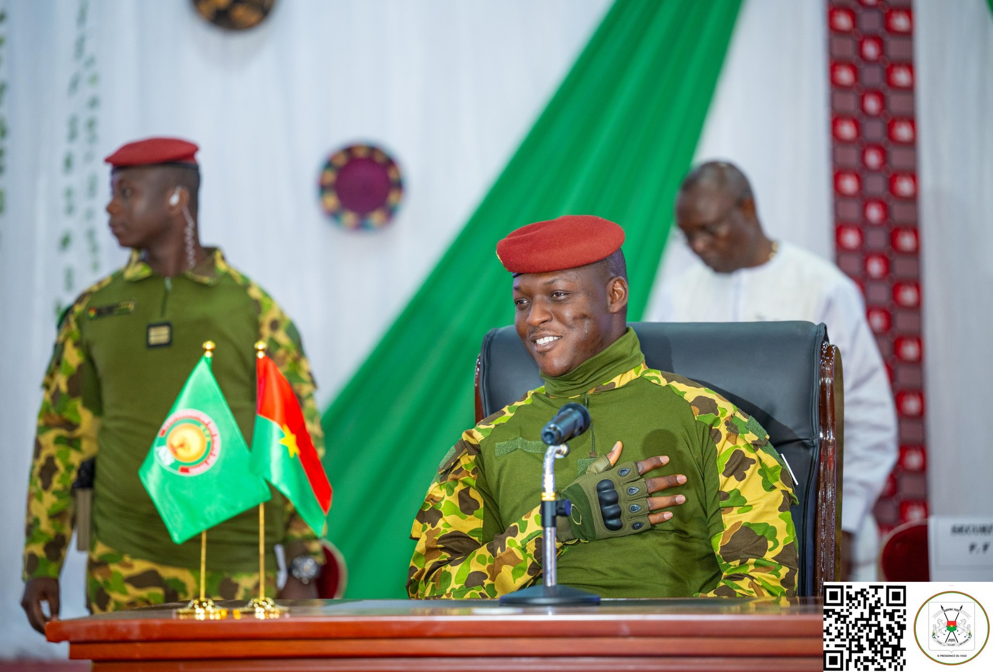 Le capitaine Ibrahim Traoré assis derrière un bureau, en tenue militaire, devant des drapeaux posés sur la table lors d’une rencontre officielle.