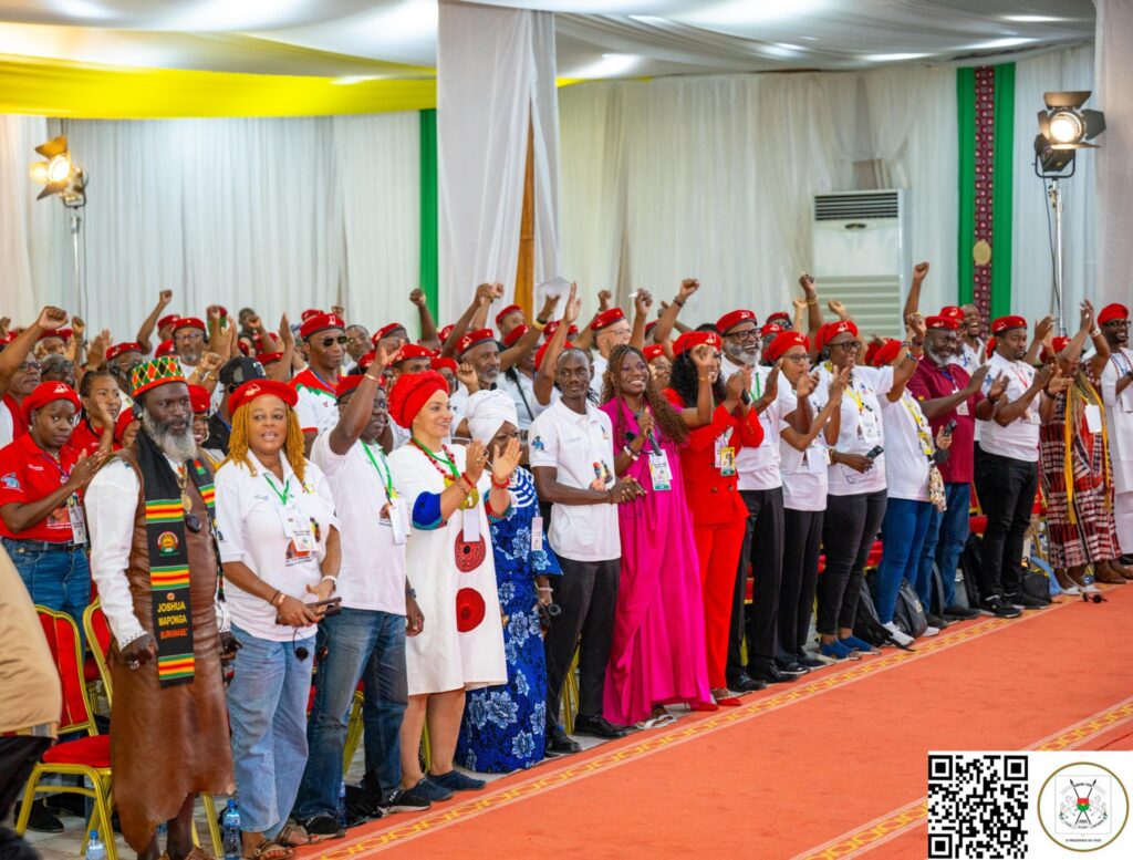 Participants debout dans une salle de conférence, applaudissant et levant le poing lors d’un rassemblement.