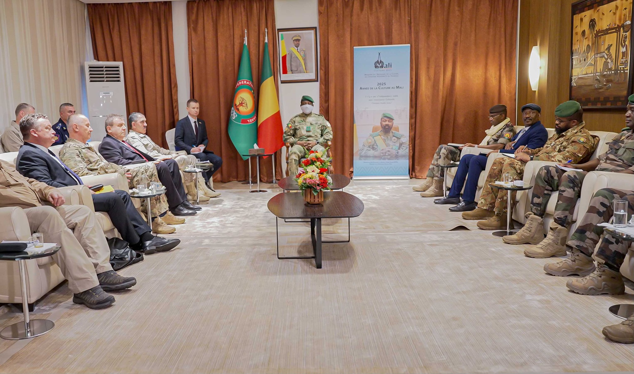 Réunion officielle entre une délégation militaire russe et des responsables militaires au Mali, assis en face à face dans une salle de conférence.