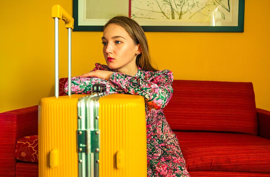 Jeune femme assise avec une valise jaune, illustrant un départ ou une expatriation.