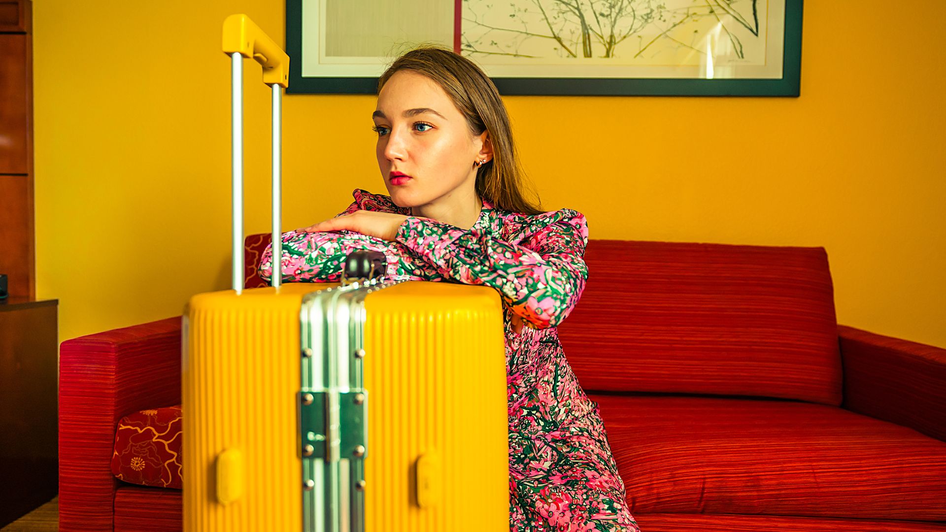 Jeune femme assise avec une valise jaune, illustrant un départ ou une expatriation.