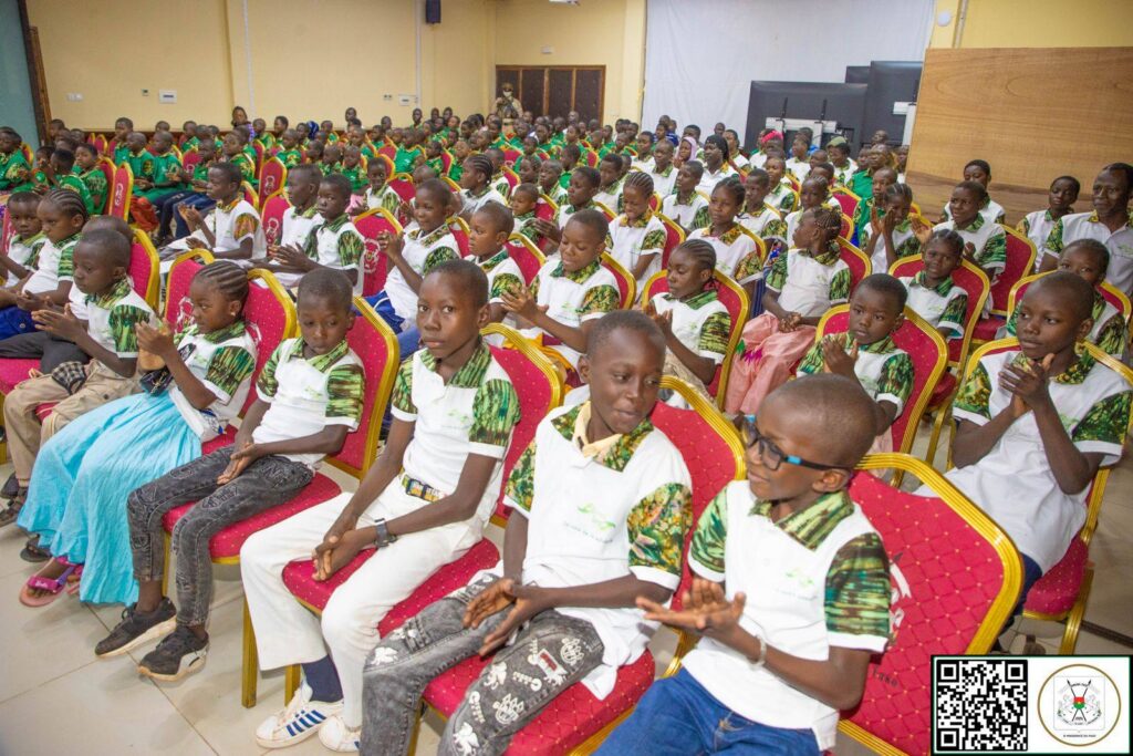 Enfants des pupilles de la Nation assis en salle, applaudissant durant l’intervention présidentielle.
